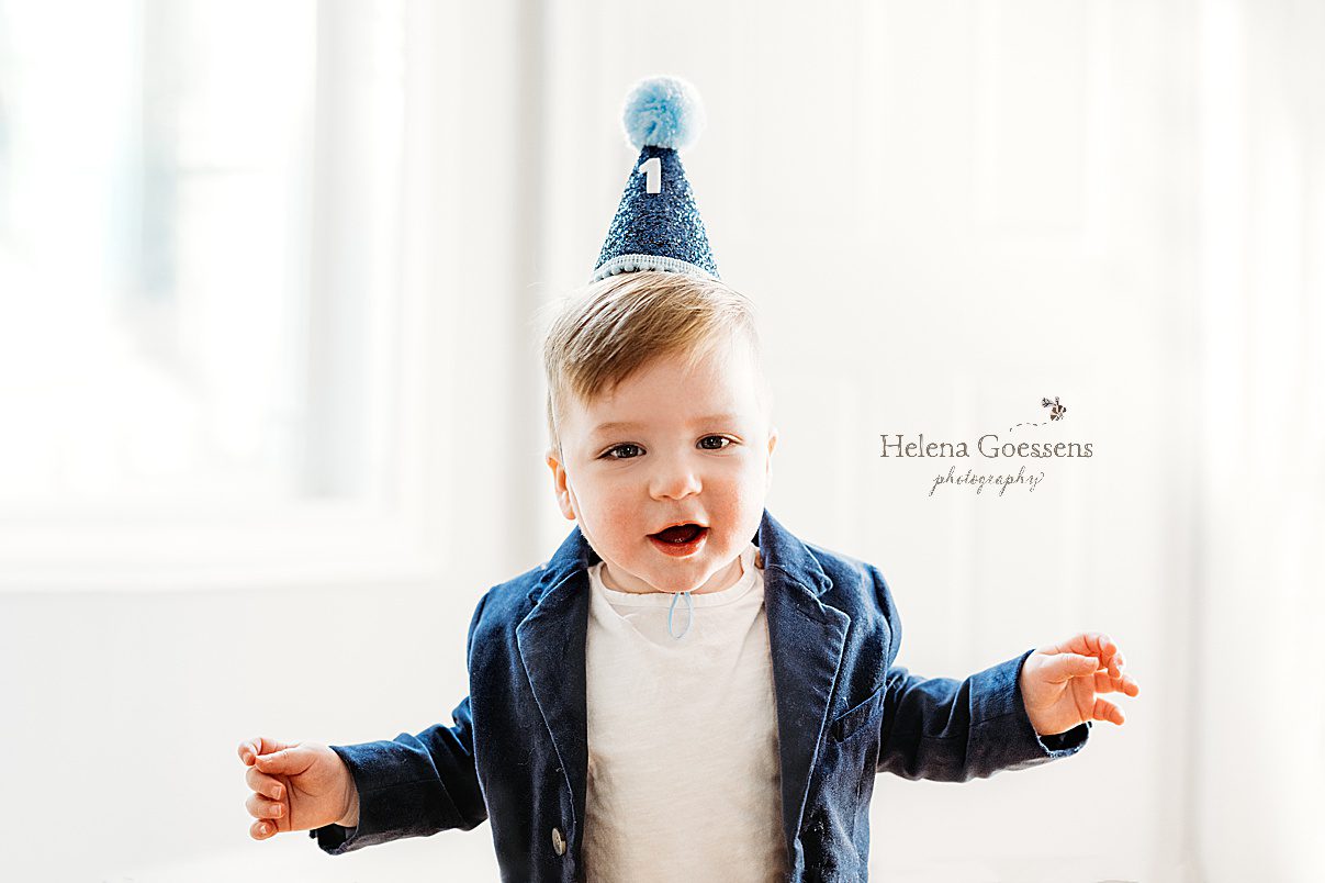 one year old poses in blue birthday hat during family photos at home 
