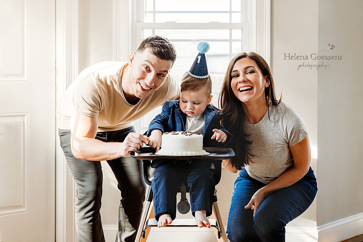 parents pose with toddler in high chair during first birthday portraits at home