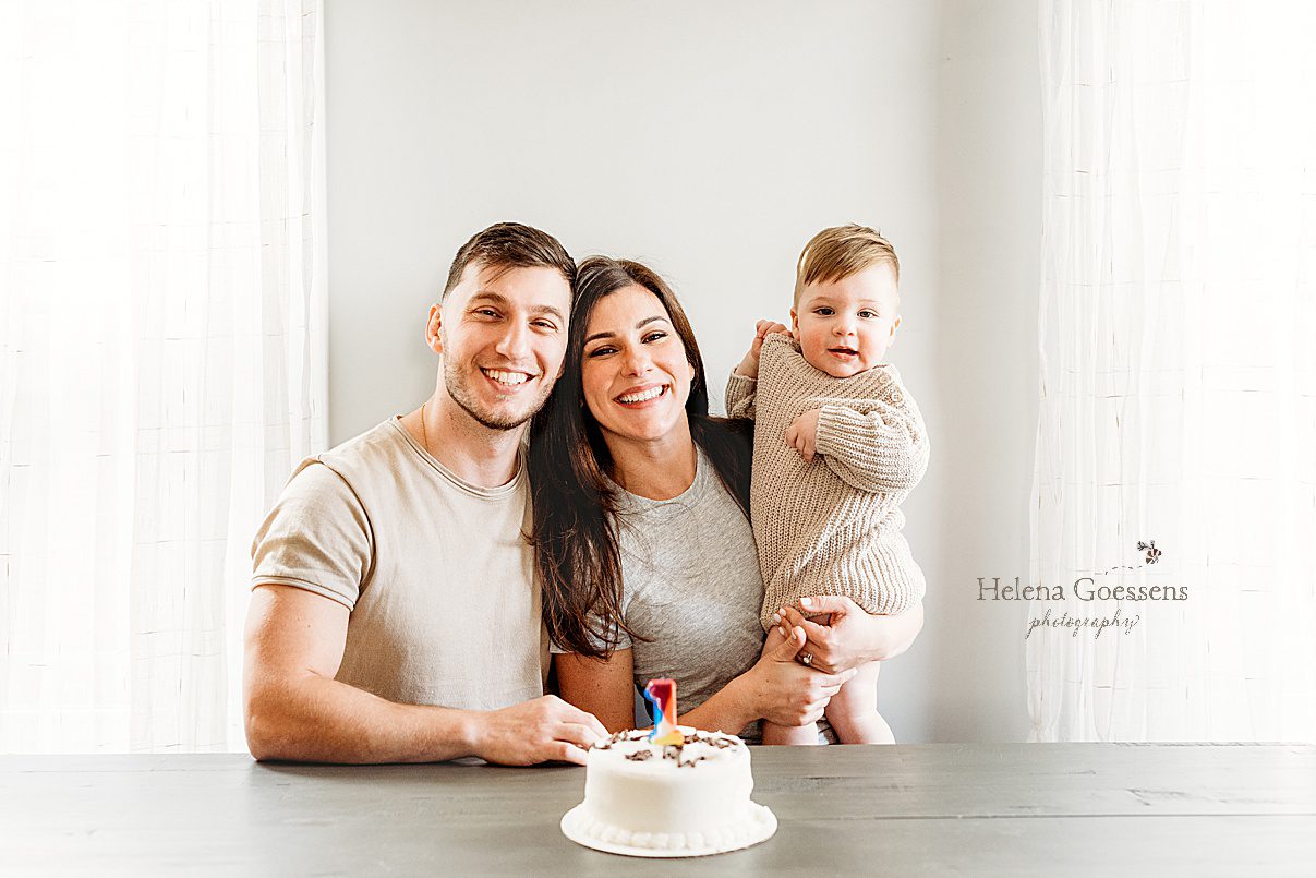 parents sit with toddler with birthday cake for first birthday portraits in Boston home
