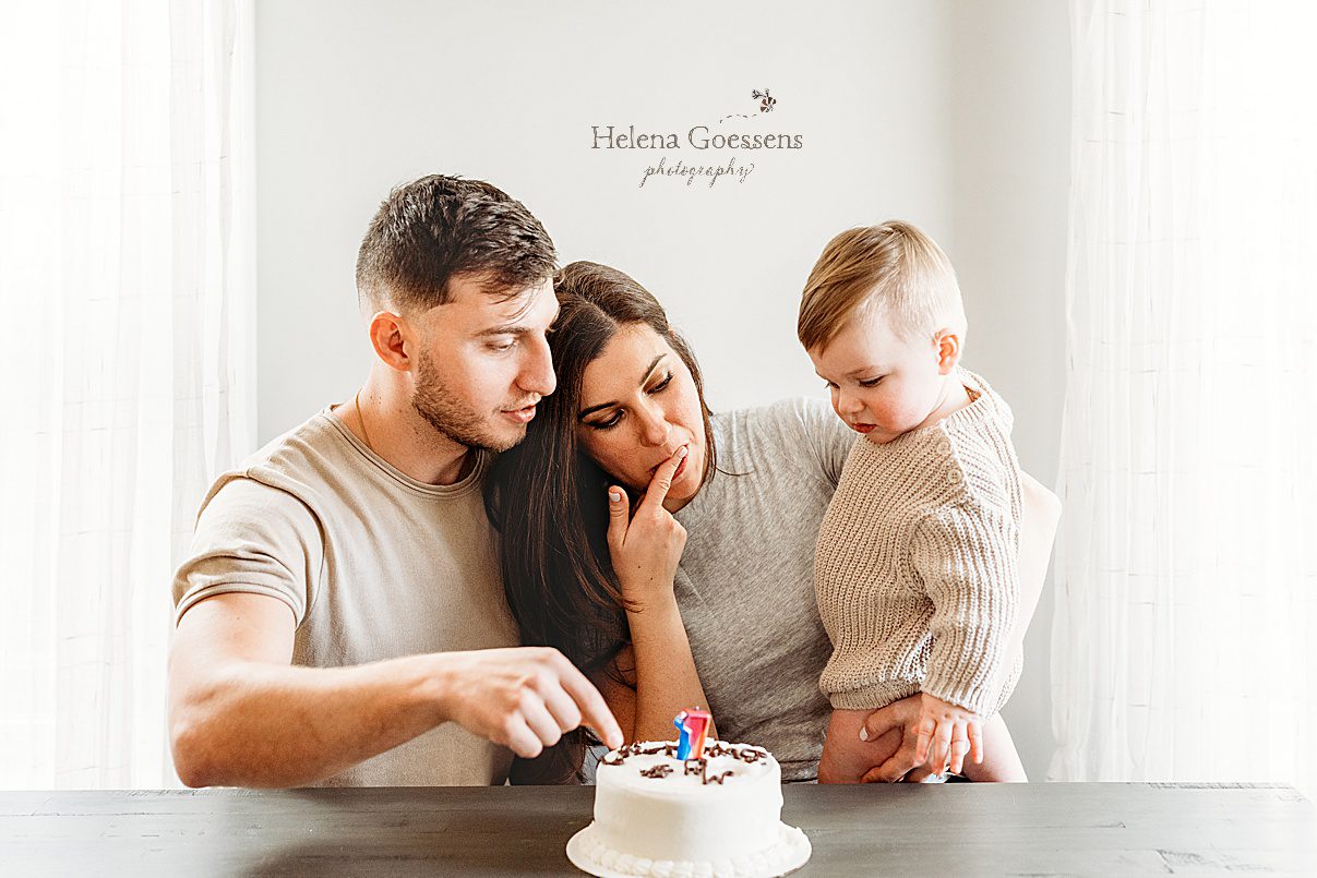 parents sit with toddler with birthday cake for first birthday portraits in Boston home
