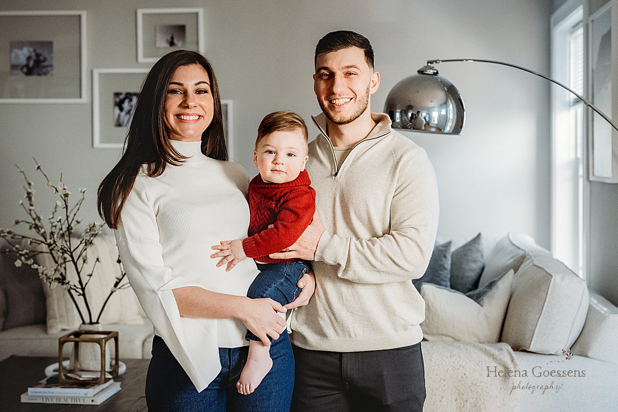 parents hold one year old on hip between them during lifestyle family photos at home in Boston MA