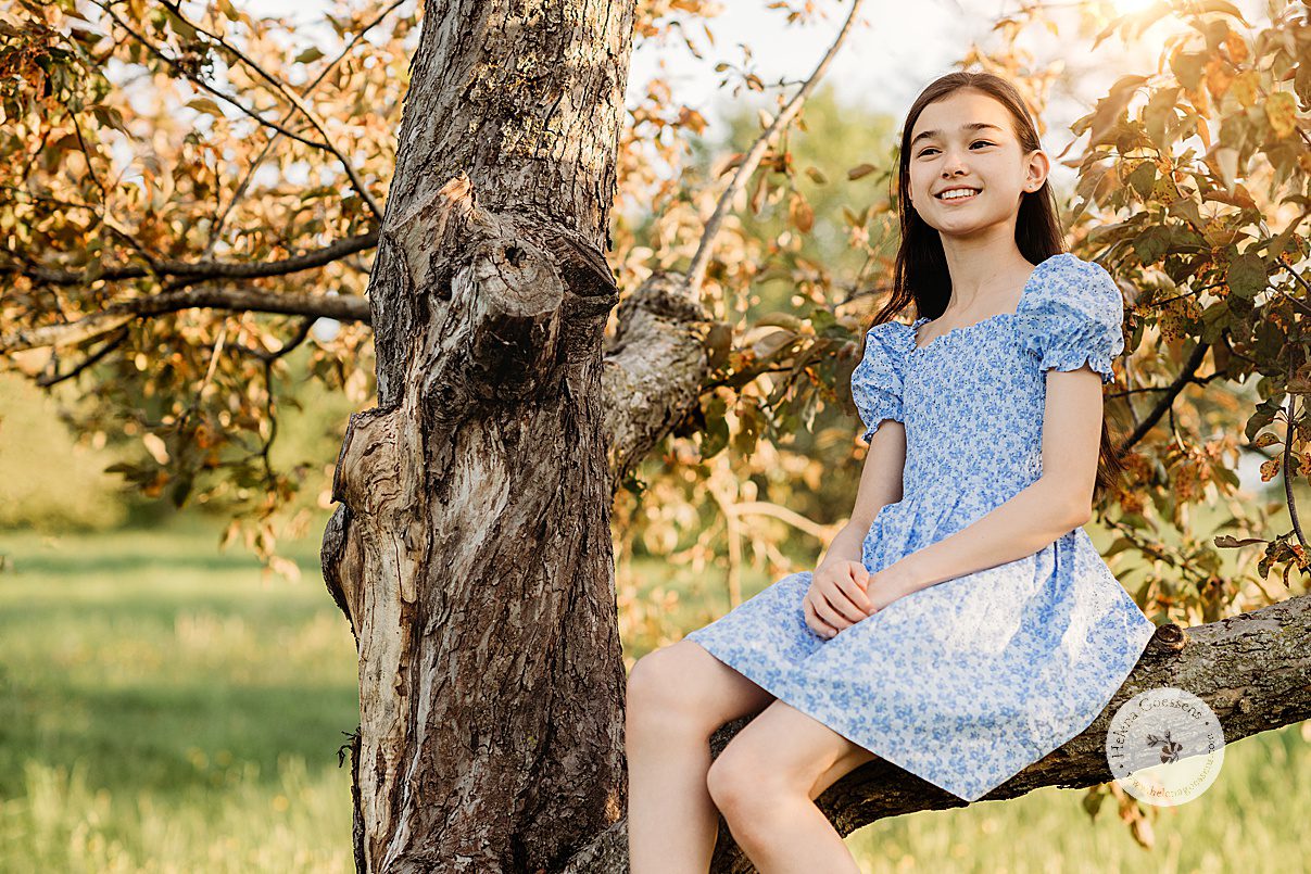 girl in blue dress sits on tree branch during Arnold Arboretum spring family photos
