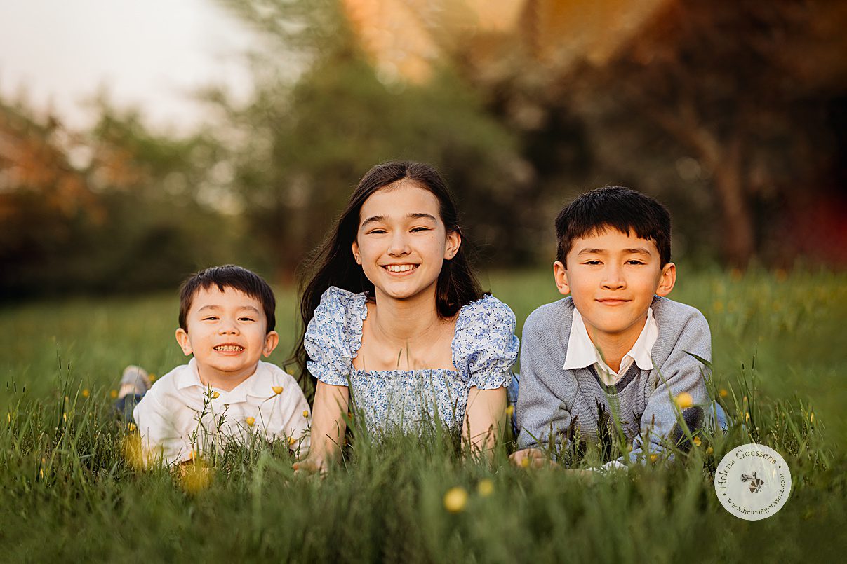 three kids lay on grass during Arnold Arboretum spring family photos