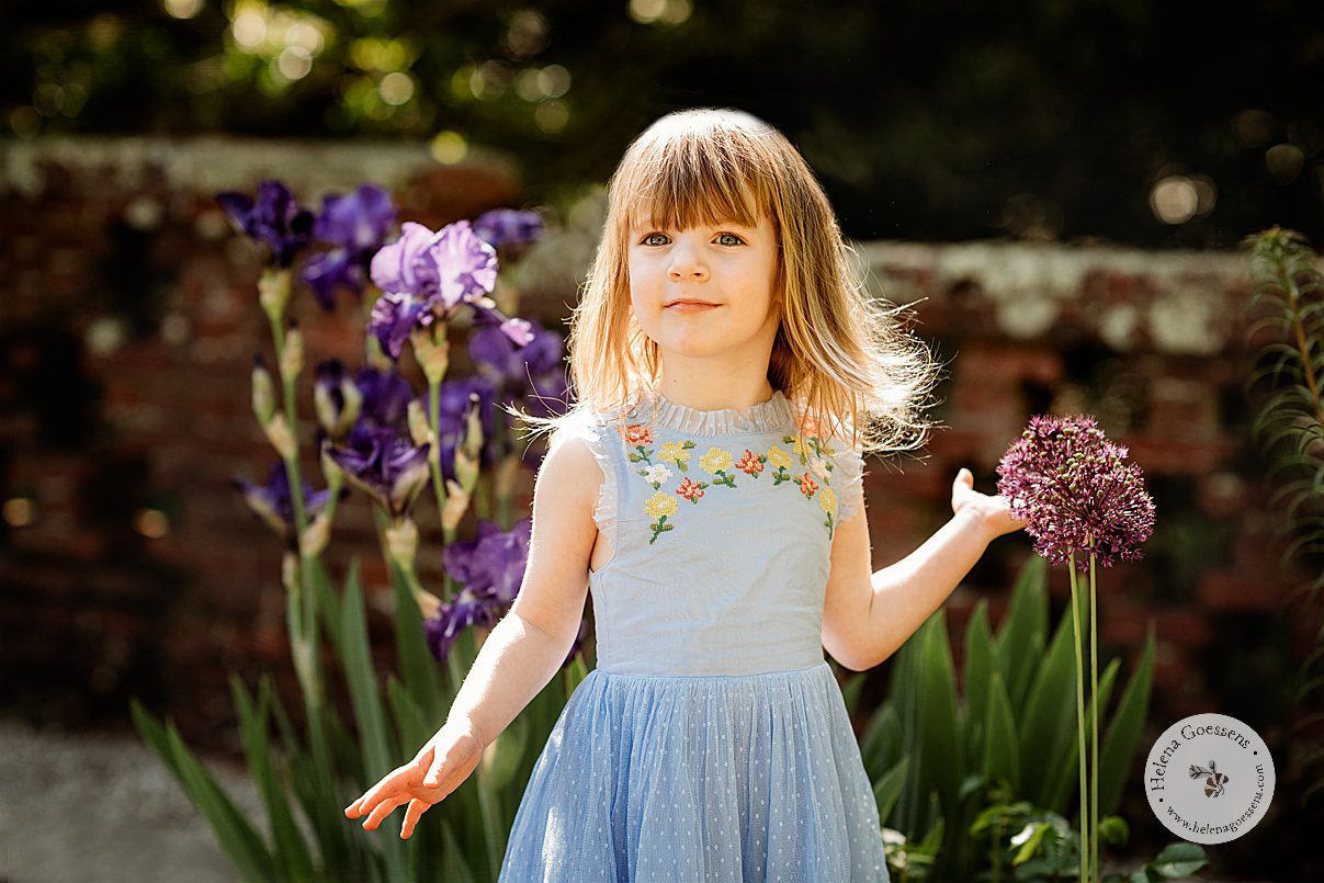 girl in blue dress with embroidered flowers plays with pink flowers during Bradley Estate family photos