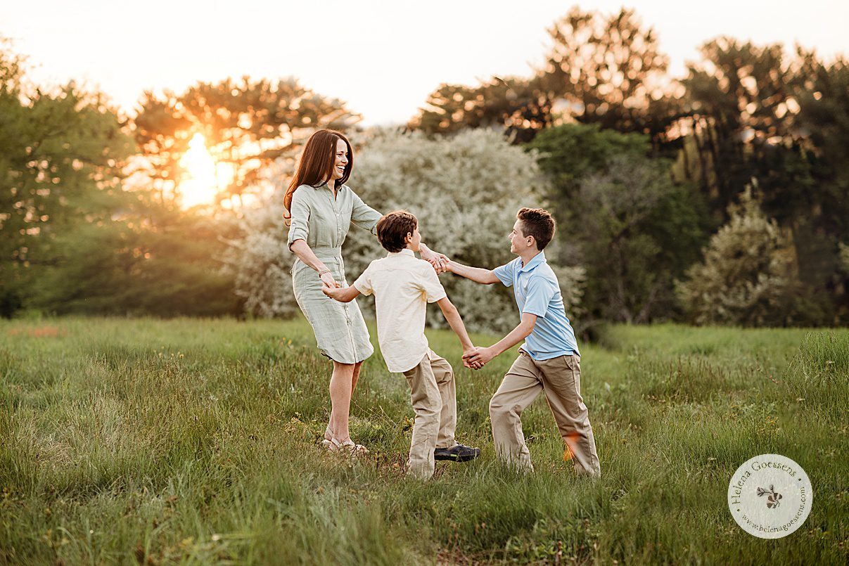 mom plays with sons in grass during family photos at Arnold Arboretum