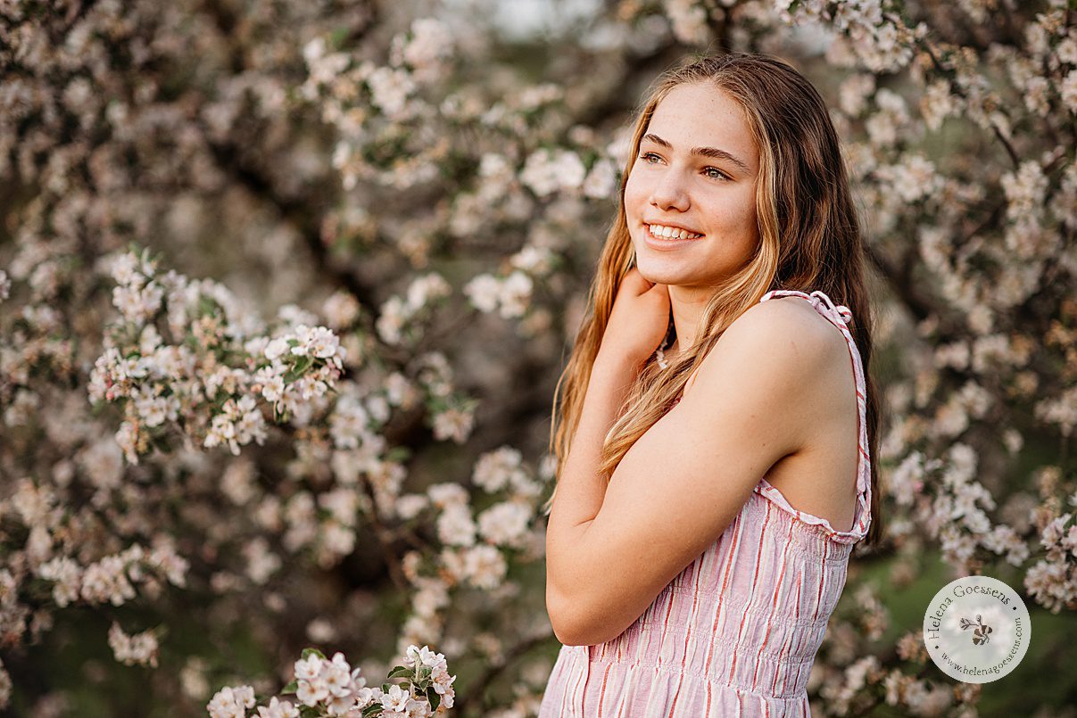 girl in pink striped dress smiles next to tree with white flowers 