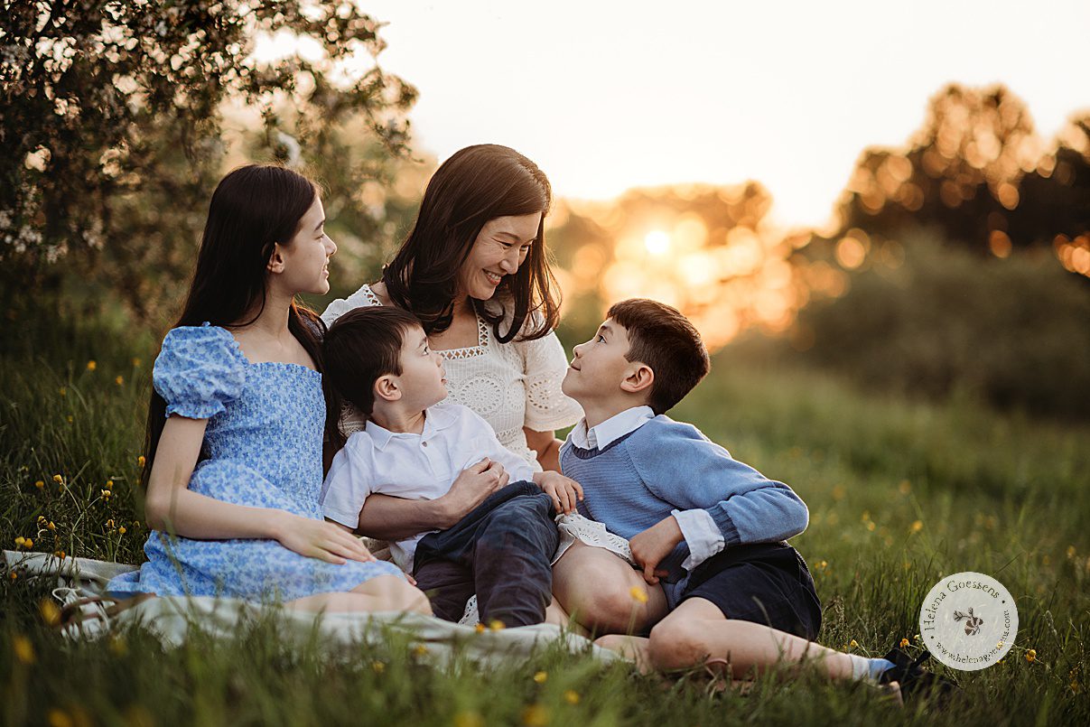 three children sit on blanket with mom at sunset in Boston park during family photos 