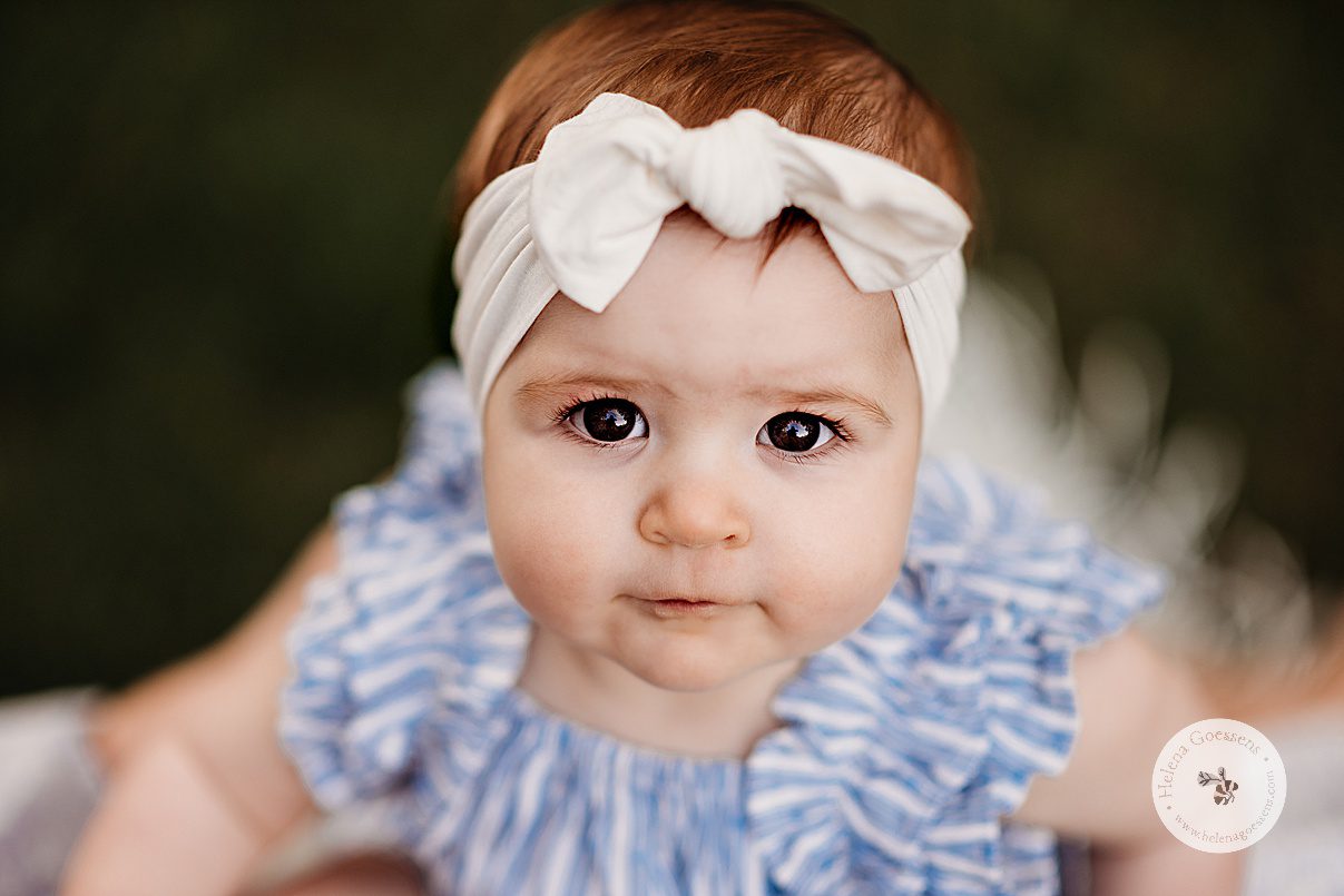 baby girl looks up at camera with white headband during family portraits at Bradley Estate