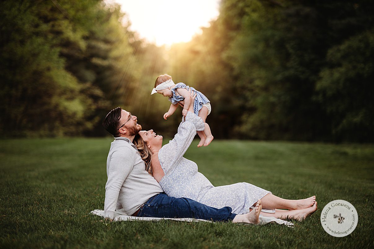 mom lifts daughter in the air leaning against husband on lawn during family portraits at Bradley Estate