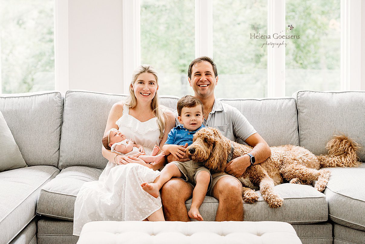 parents sit with toddler son, new baby girl and dog on couch in Westwood MA home