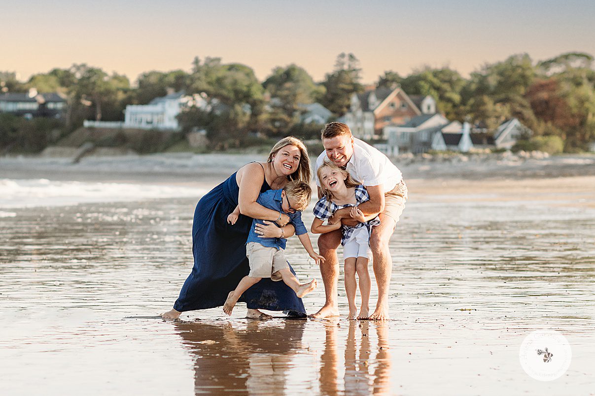 parents stand holding kids in water during beach family portraits in Swampscott MA