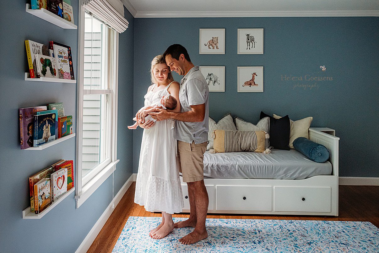 parents hug daughter standing by window in nursery during lifestyle newborn photos in Westwood MA