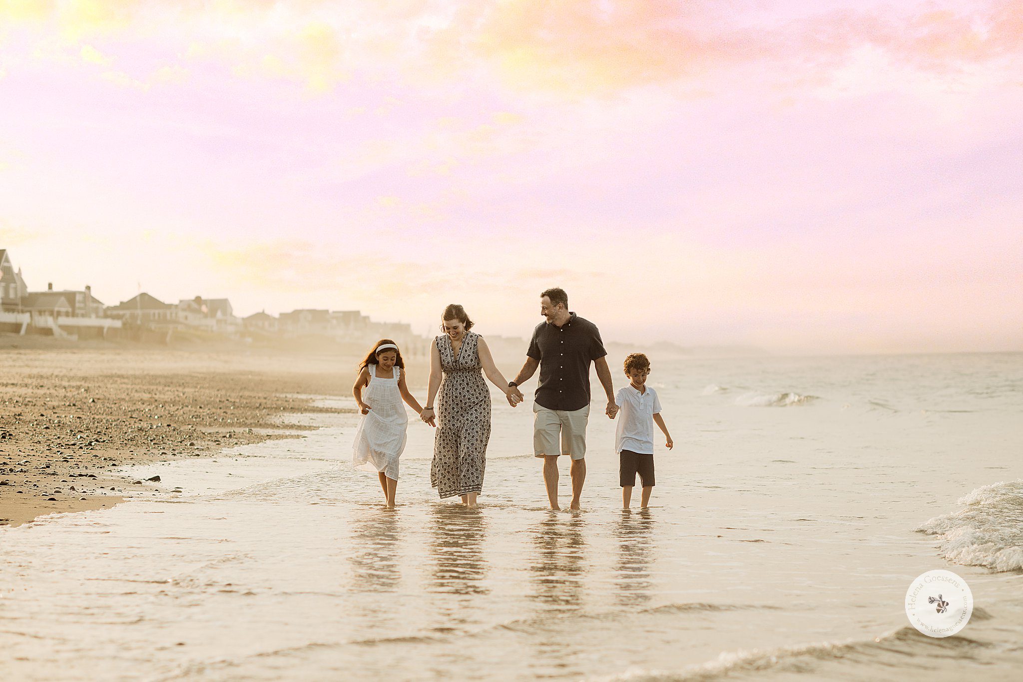 family of four holds hands walking through water on beach during Marshfield family portraits