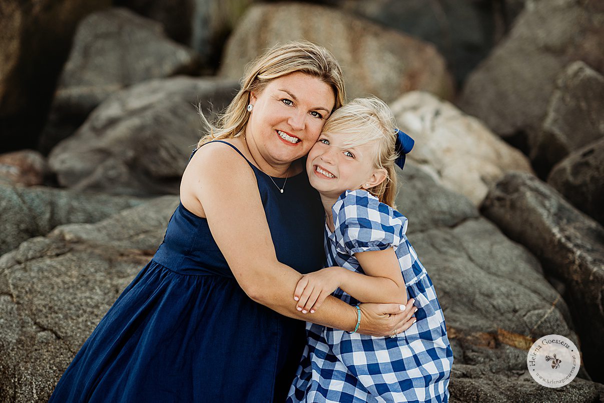 woman hugs daughter sitting on rocks during beach family portraits in Swampscott MA