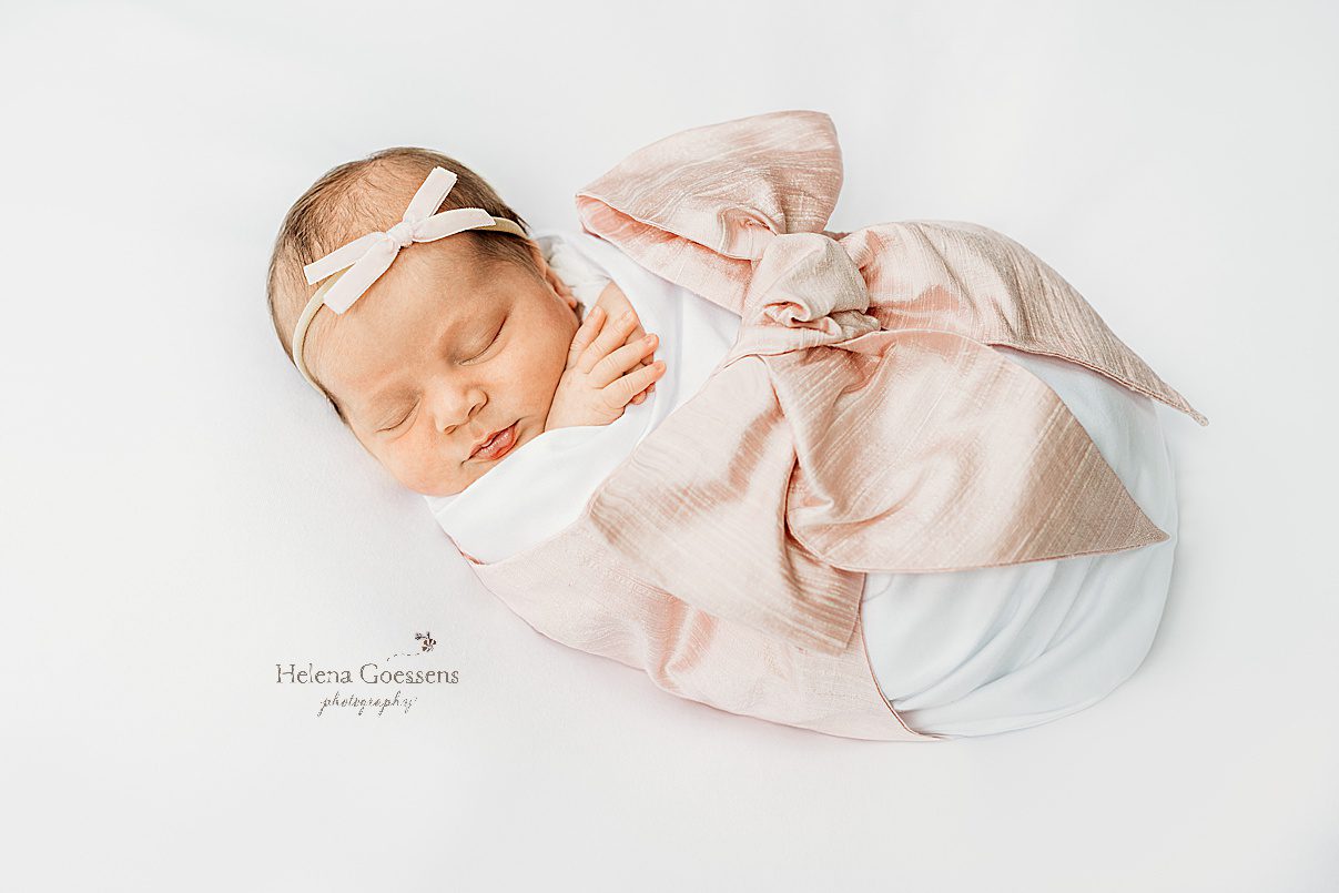 baby lays in white wrap with large pink bow around her 