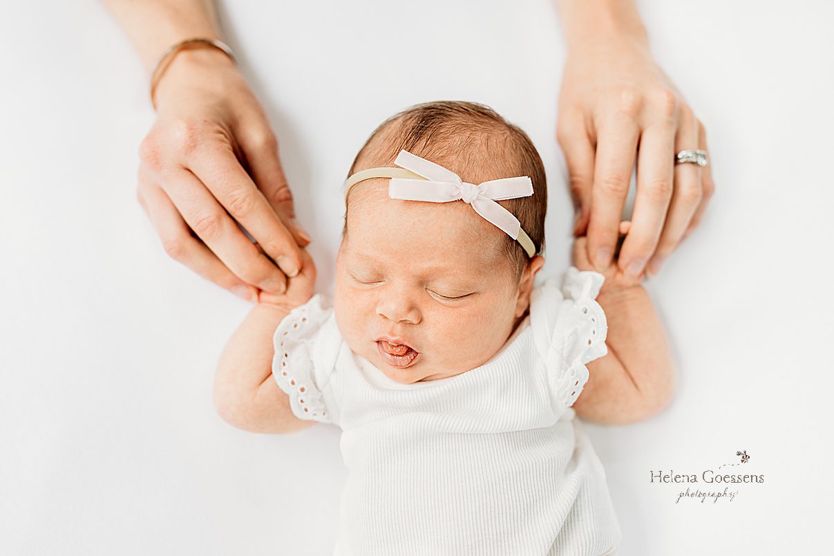 mom holds baby's hands while she lays on white sheet during newborn photos at home 