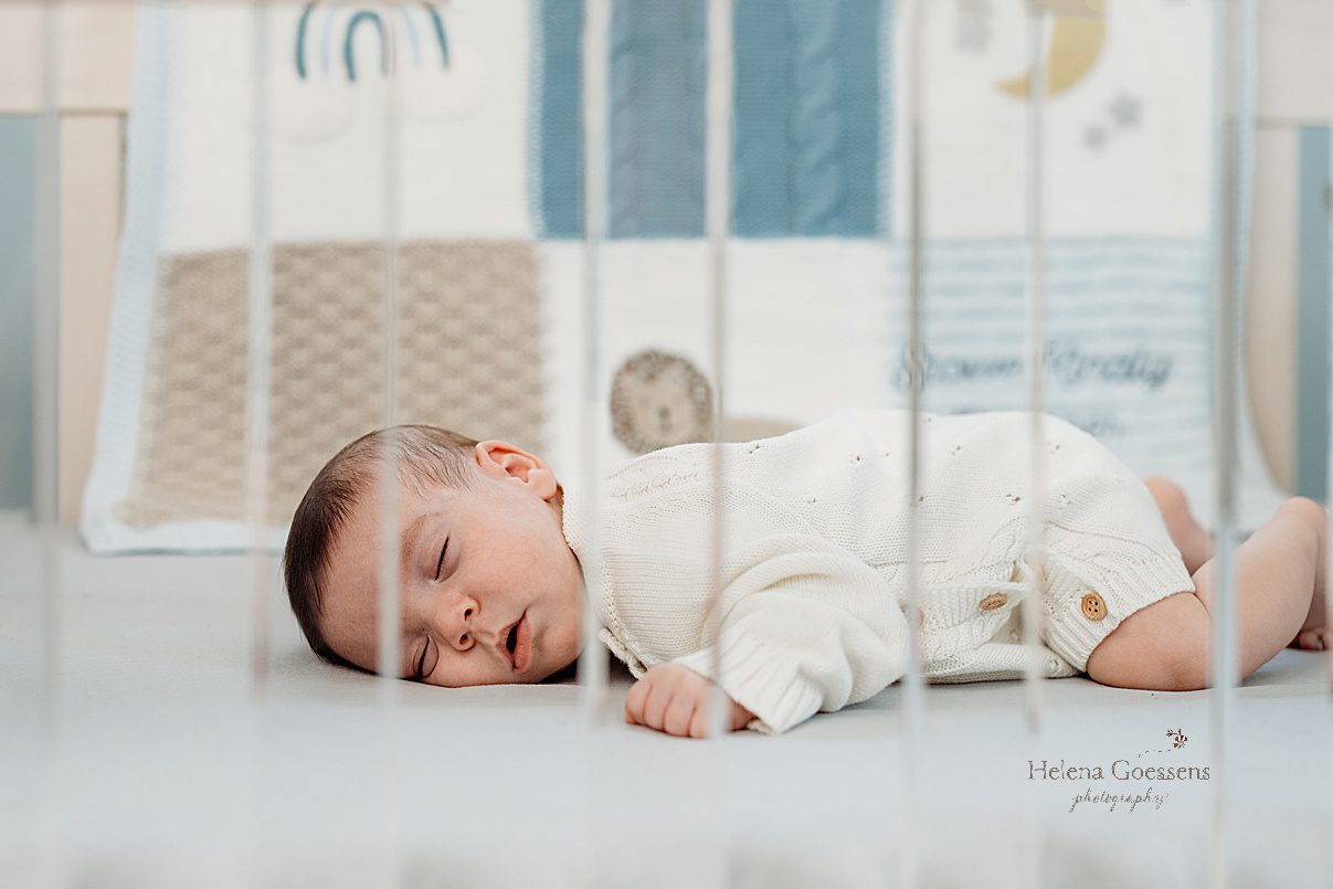 baby boy sleeps on stomach in crib in hand knit white sweater during lifestyle newborn portraits in Westwood MA