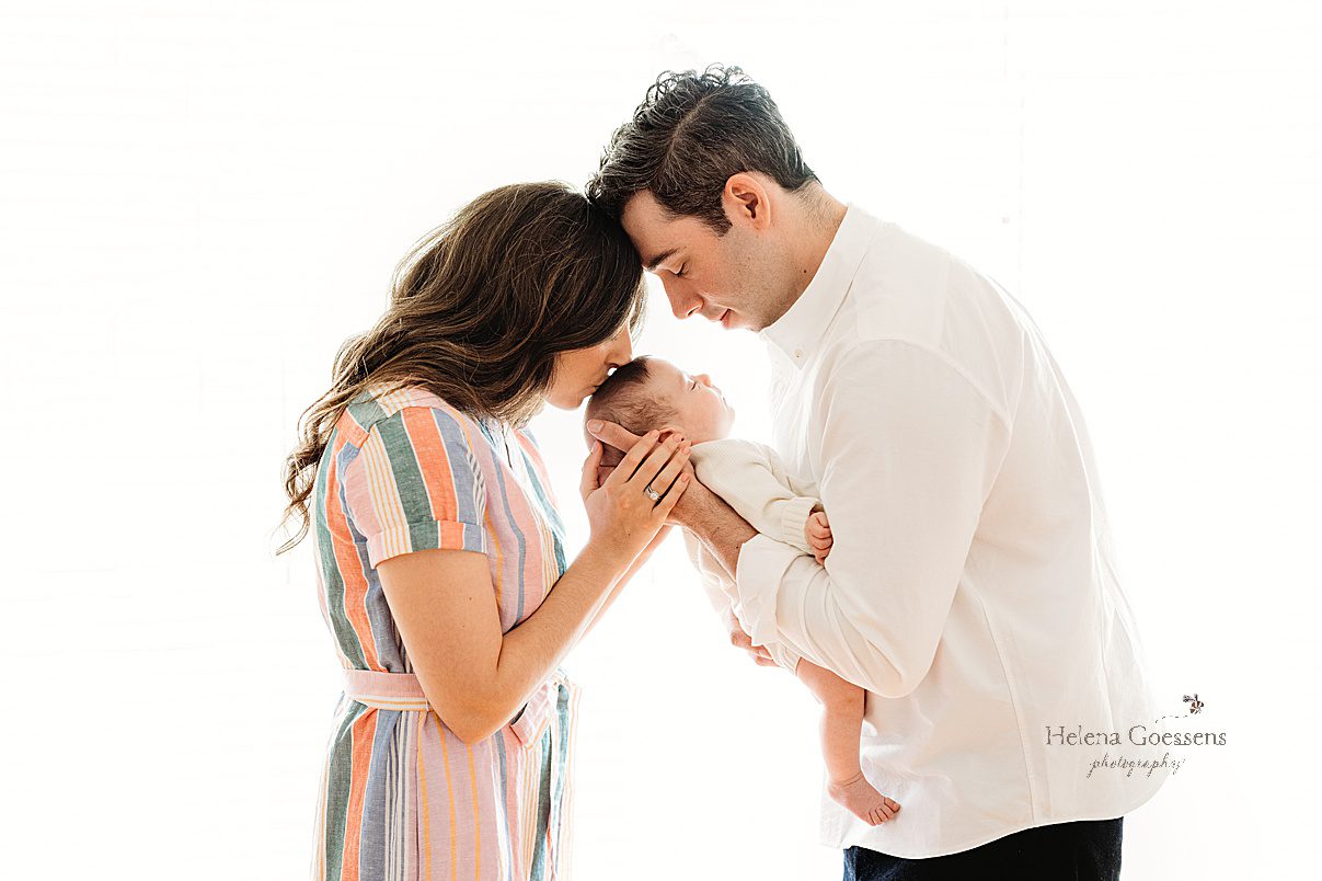 new parents lean over son touching heads together during lifestyle newborn portraits in Westwood MA