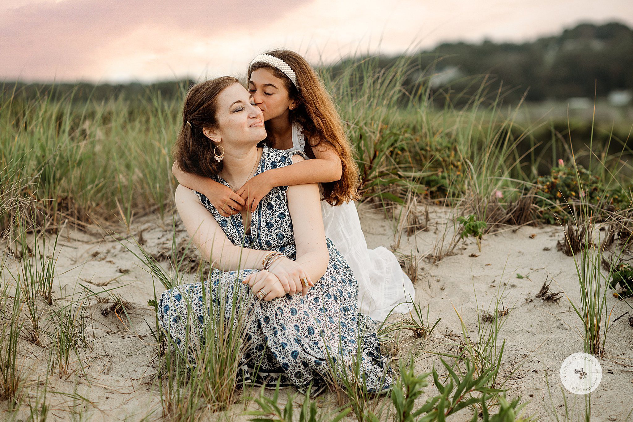 daughter in white hugs mom from behind on sand dune during Marshfield family portraits on the beach 