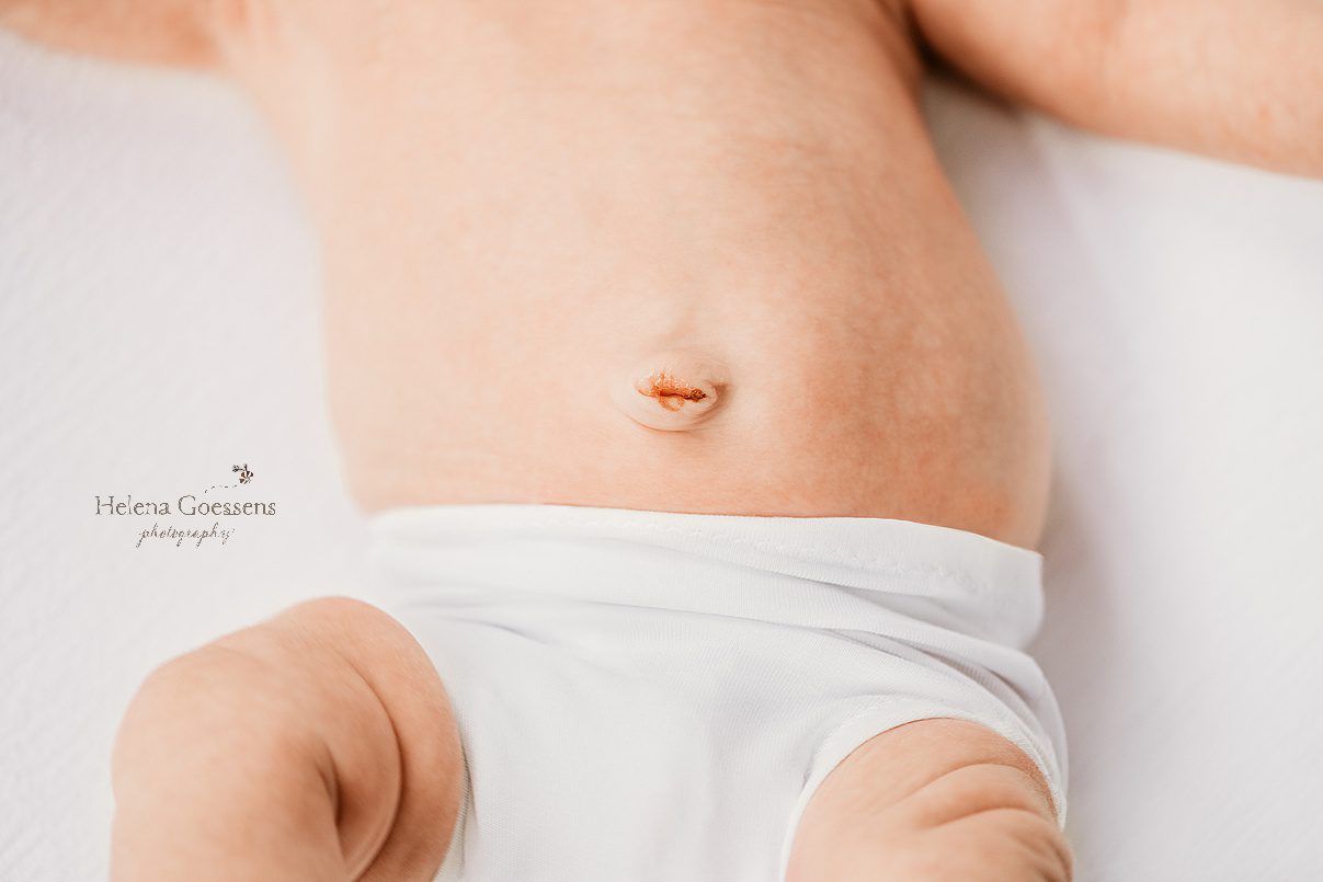 close up of baby's belly with dried umbilical cord above white diaper cover 