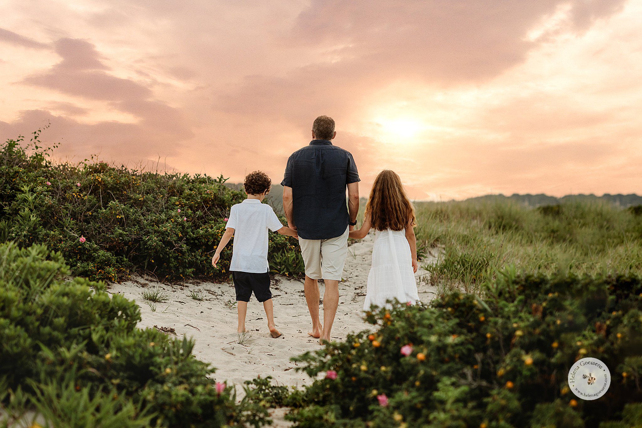 dad holds hands with two kids walking on dunes during Marshfield family portraits