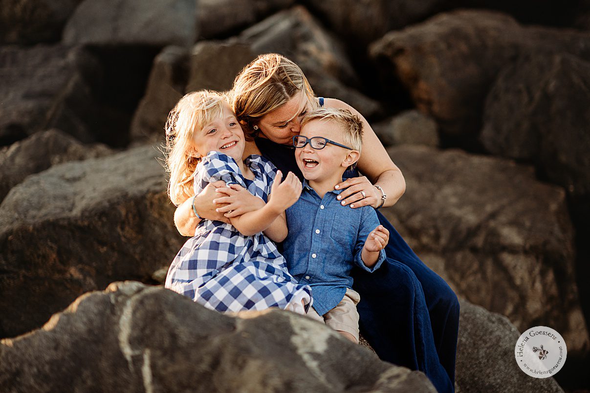 mom in navy gown kisses son while hugging him and his sister on rocks in  Swampscott MA