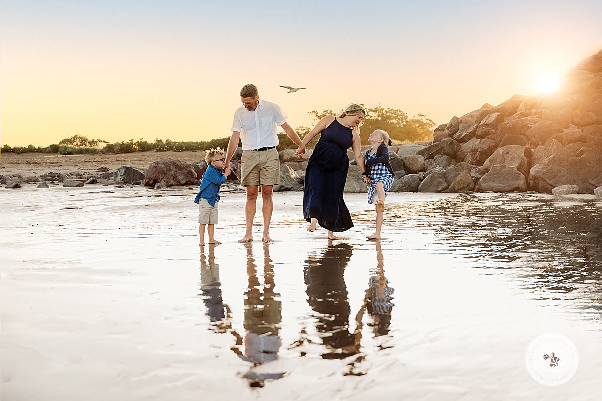 family of four holds hands walking through water at low tide during beach family portraits in Swampscott MA
