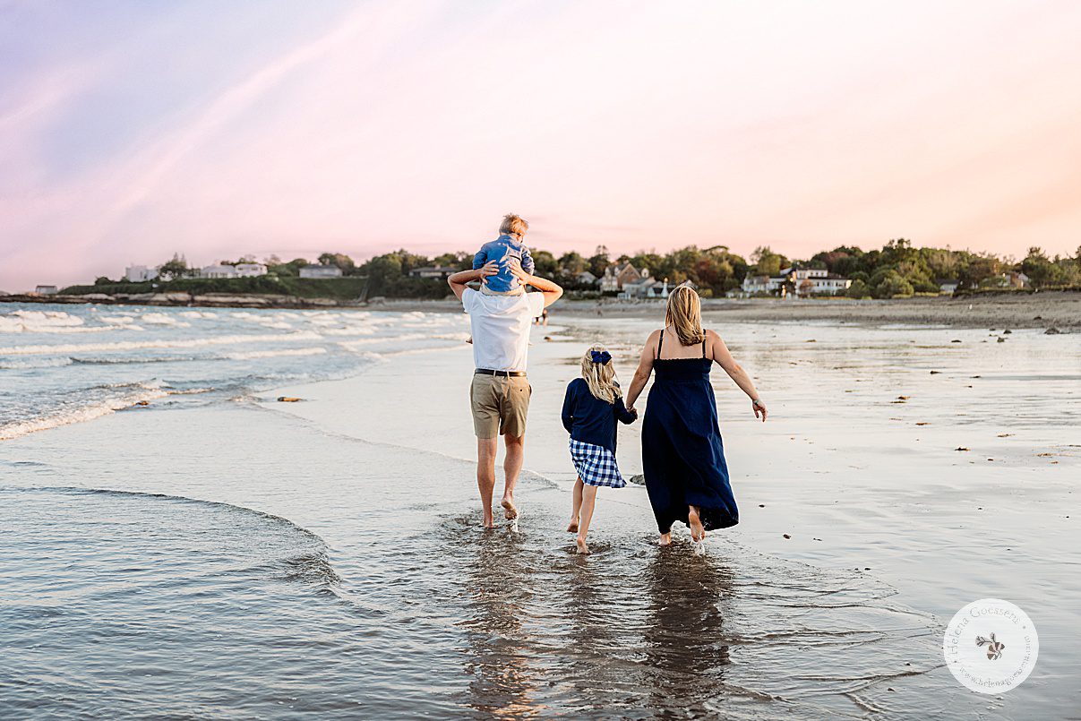 mom in navy gown holds daughter's hand walking through water on Boston MA beach