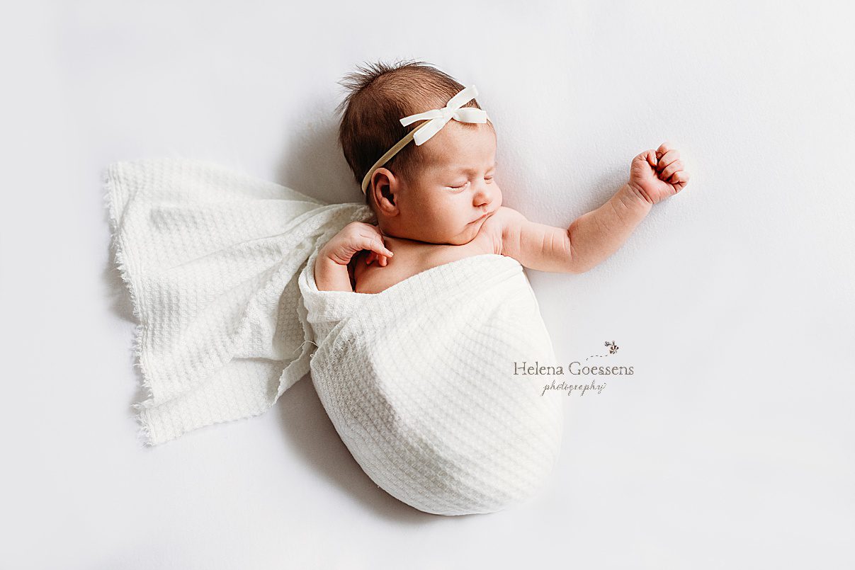 baby girl in white wrap with white headband lays on blanket during newborn photos in MA