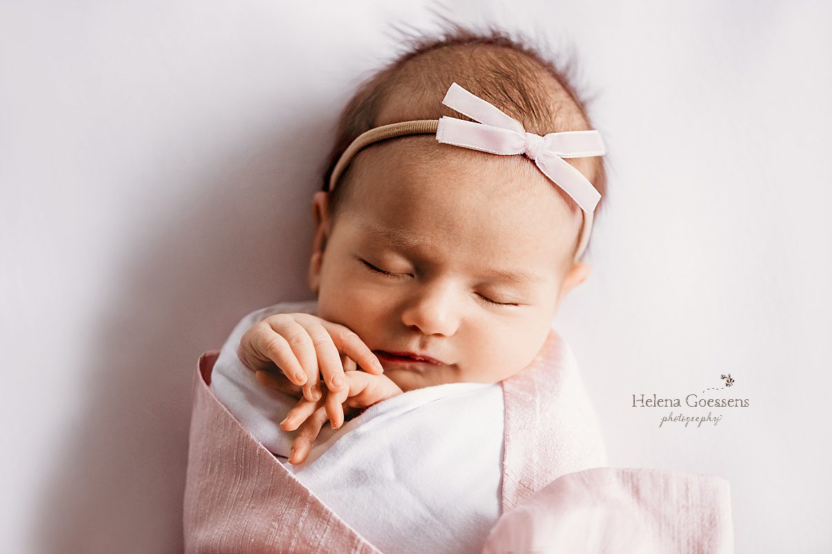 baby girl with pink wrap and pink bow lays on bed during Needham MA lifestyle newborn portraits