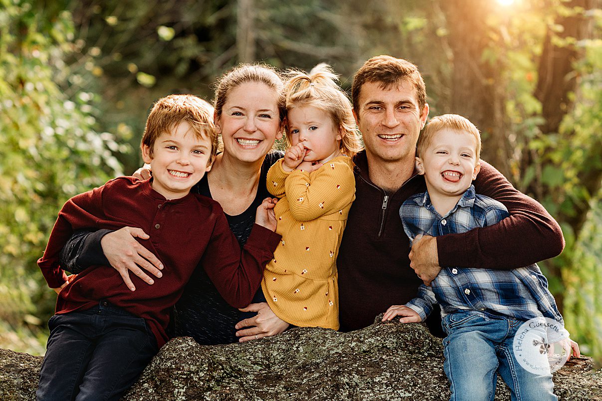 family of five hugs on log during fall Larz Anderson Park family portraits in mustard, burgundy and navy outfits 