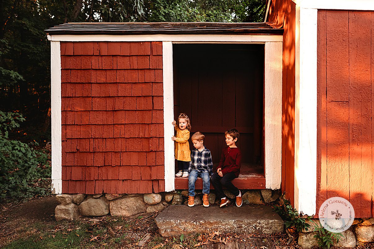 three kids climb in red shed during Larz Anderson Park family portraits
