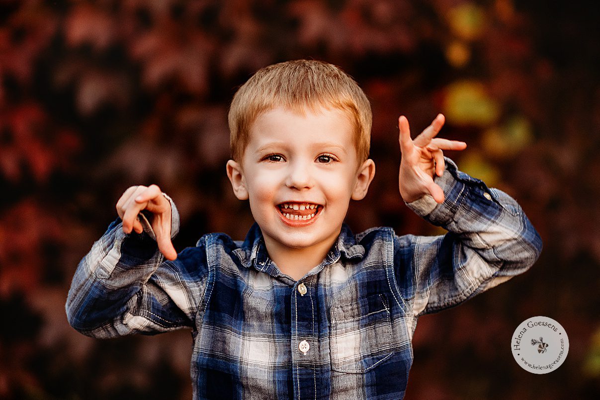 blonde boy makes funny face in blue plaid shirt during fall Boston family portraits