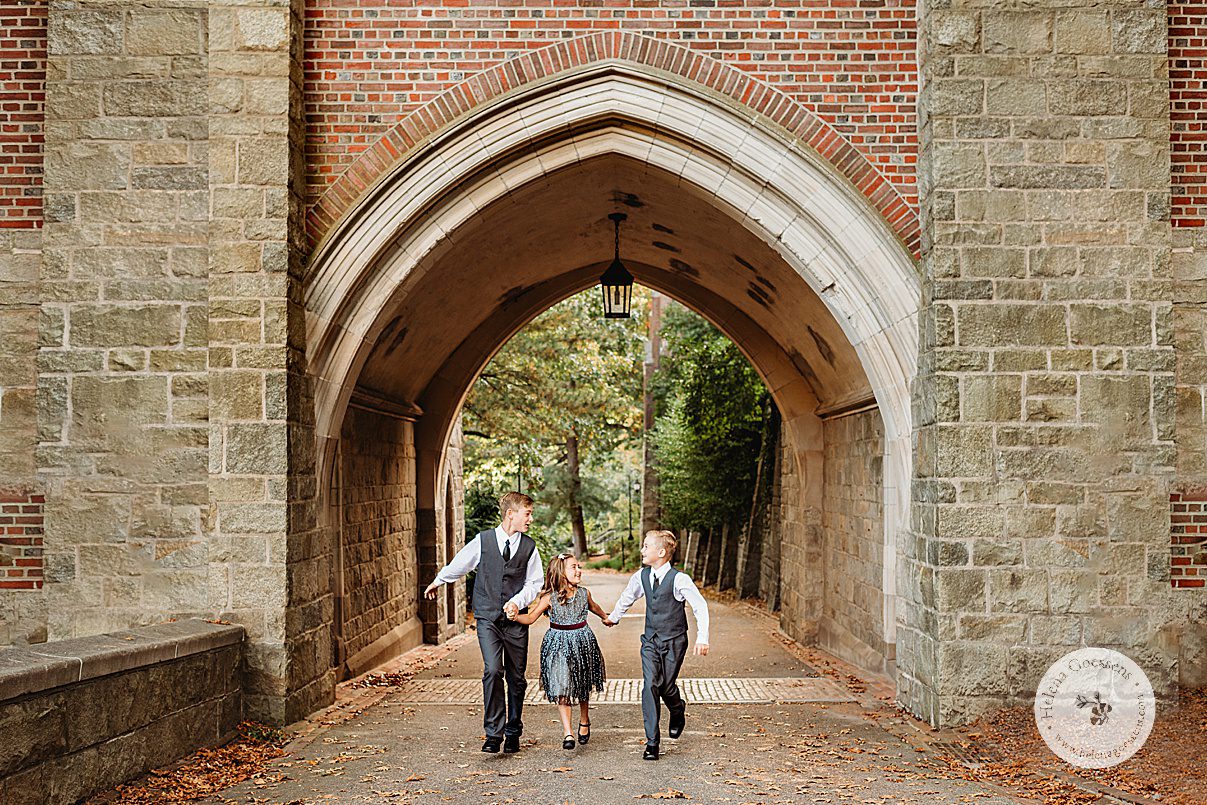 three siblings hold hands running through stone archway at Wellesley College