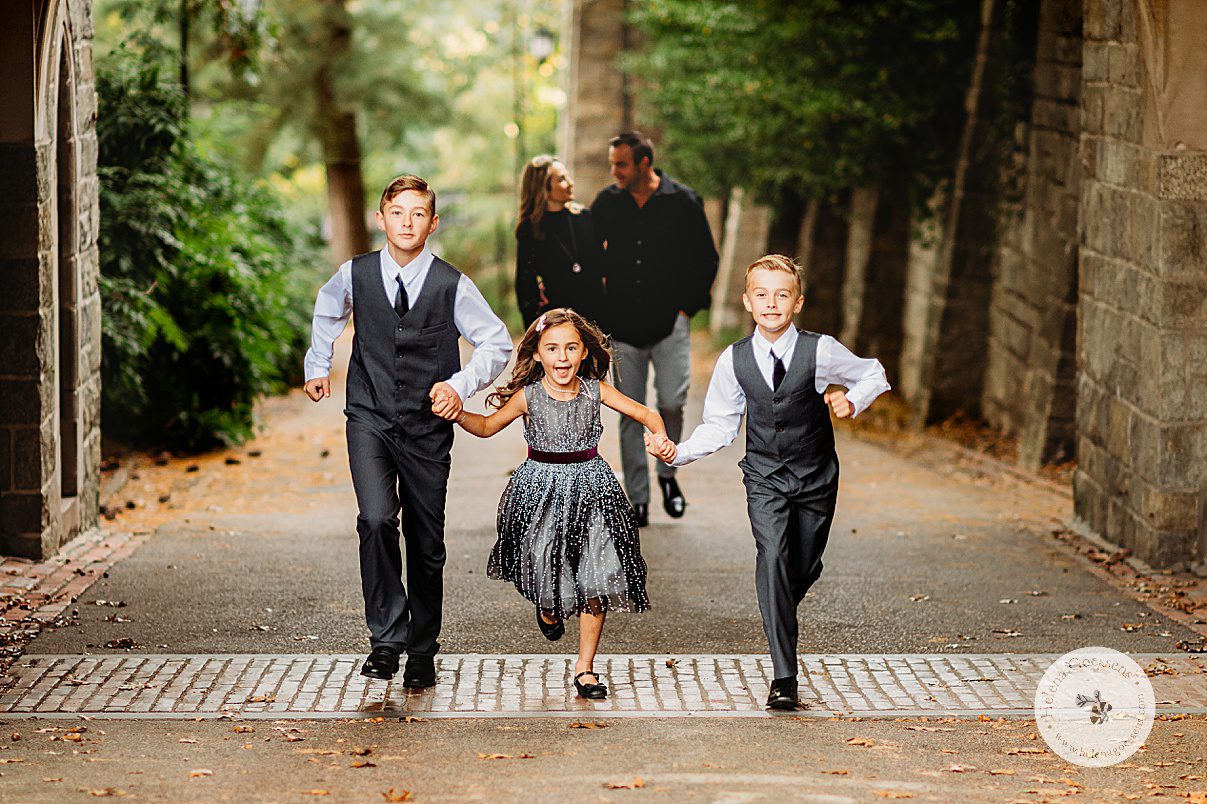 three kids hold hands running while parents walk behind them during fall family photos in Boston MA