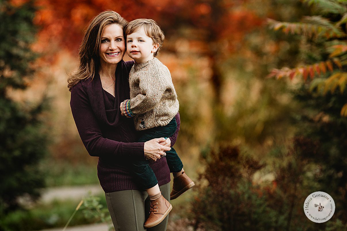 mom in plum sweater hugs toddler in tan sweater during fall family portraits at Wellesley College