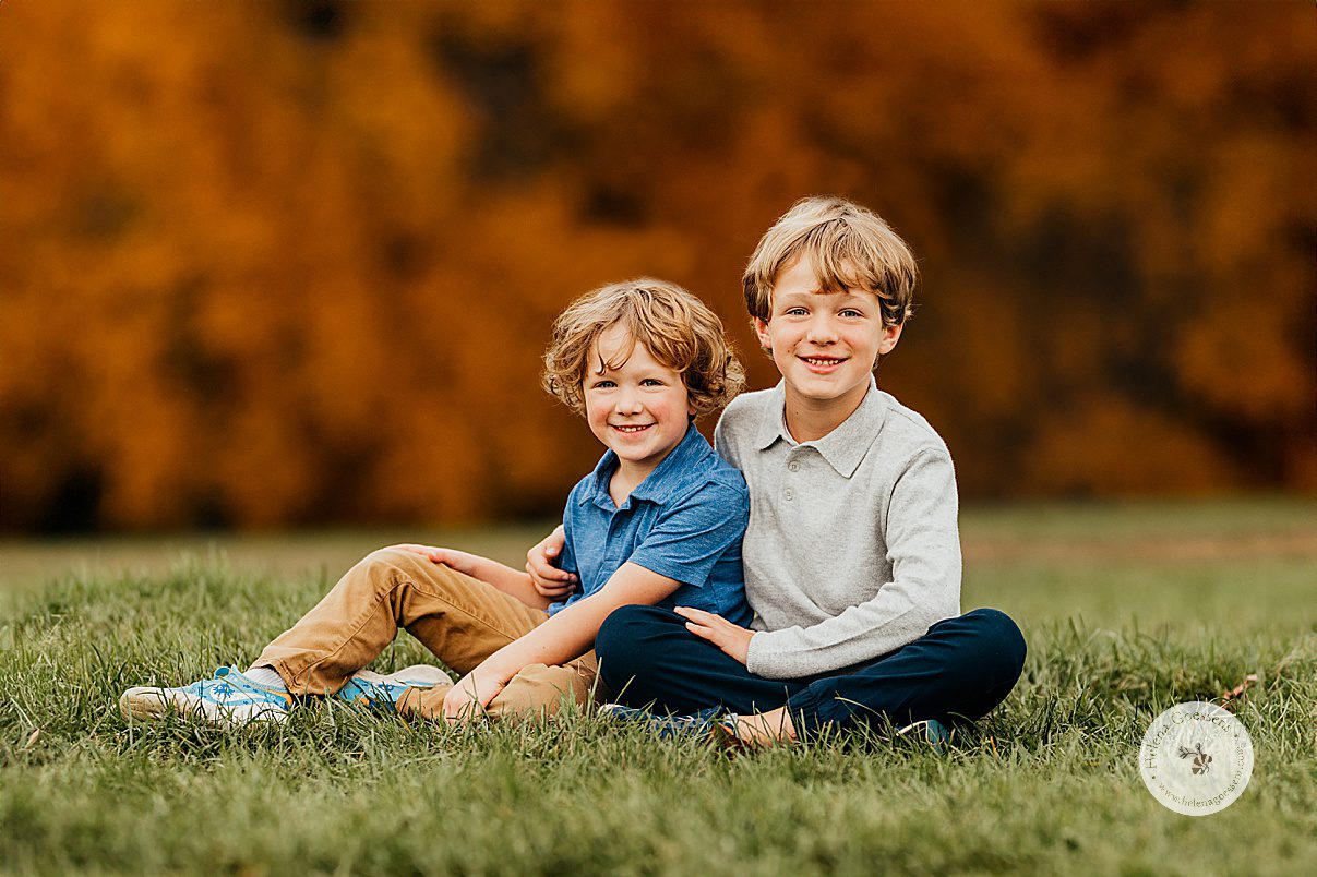 brothers sit on lawn during fall family portraits at Larz Anderson Park