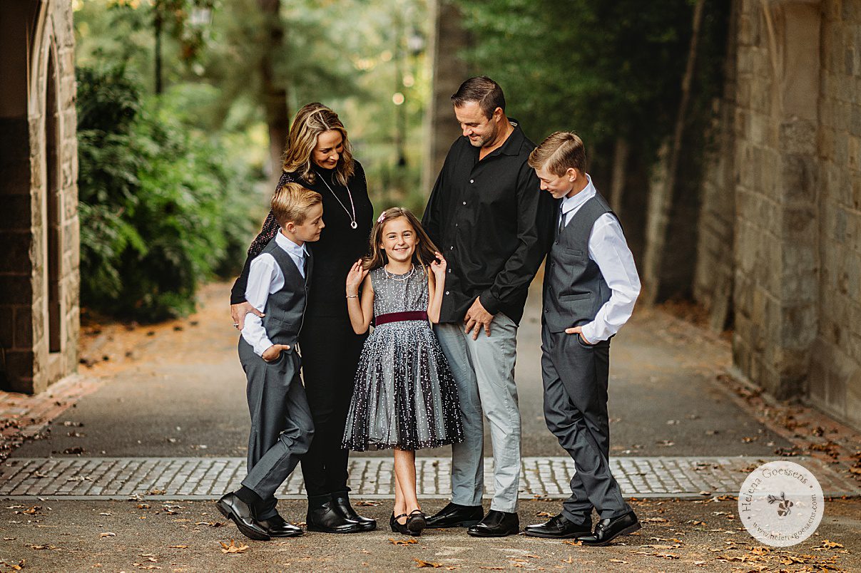 parents smile down at daughter in black and white dress moving hair while hugging sons