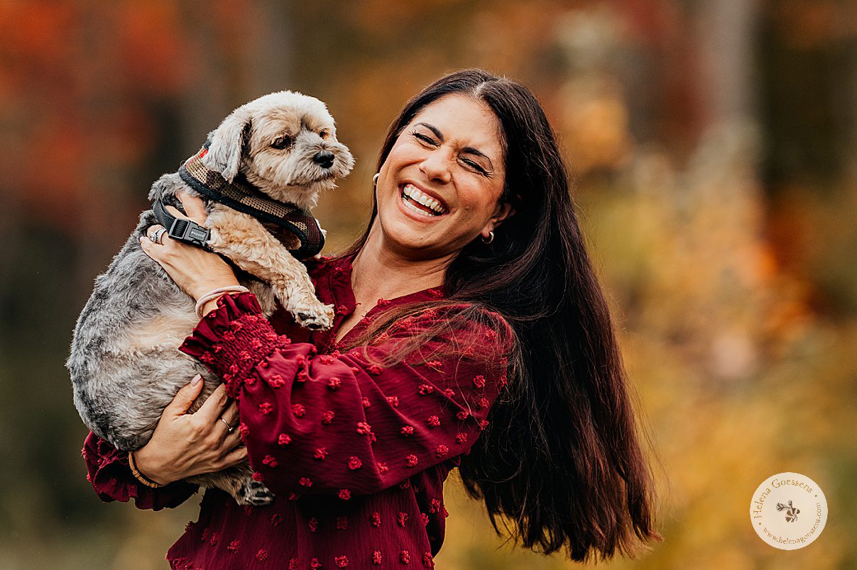 mom laughs while holding small dog during fall lifestyle family portraits in Westwood MA