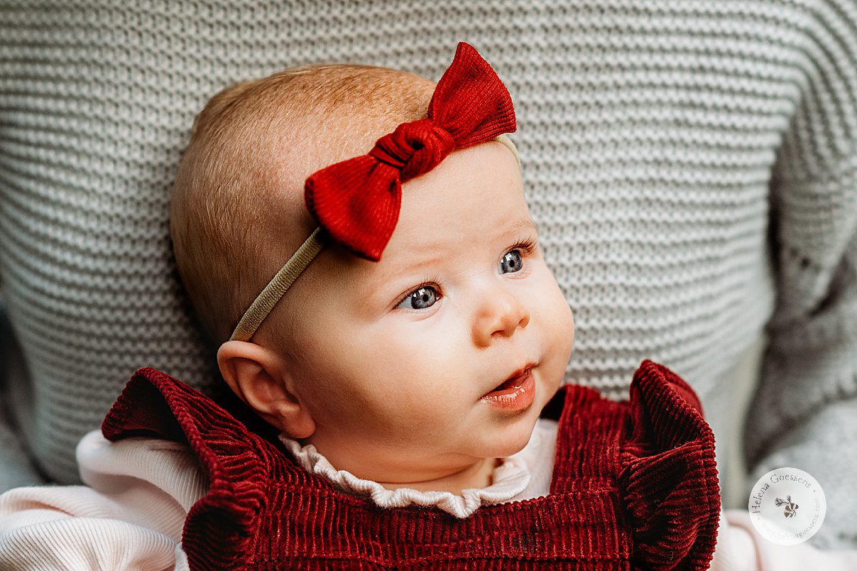 baby girl in red corduroy dress with matching bow looks away from mom during fall family photos at Wellesley College