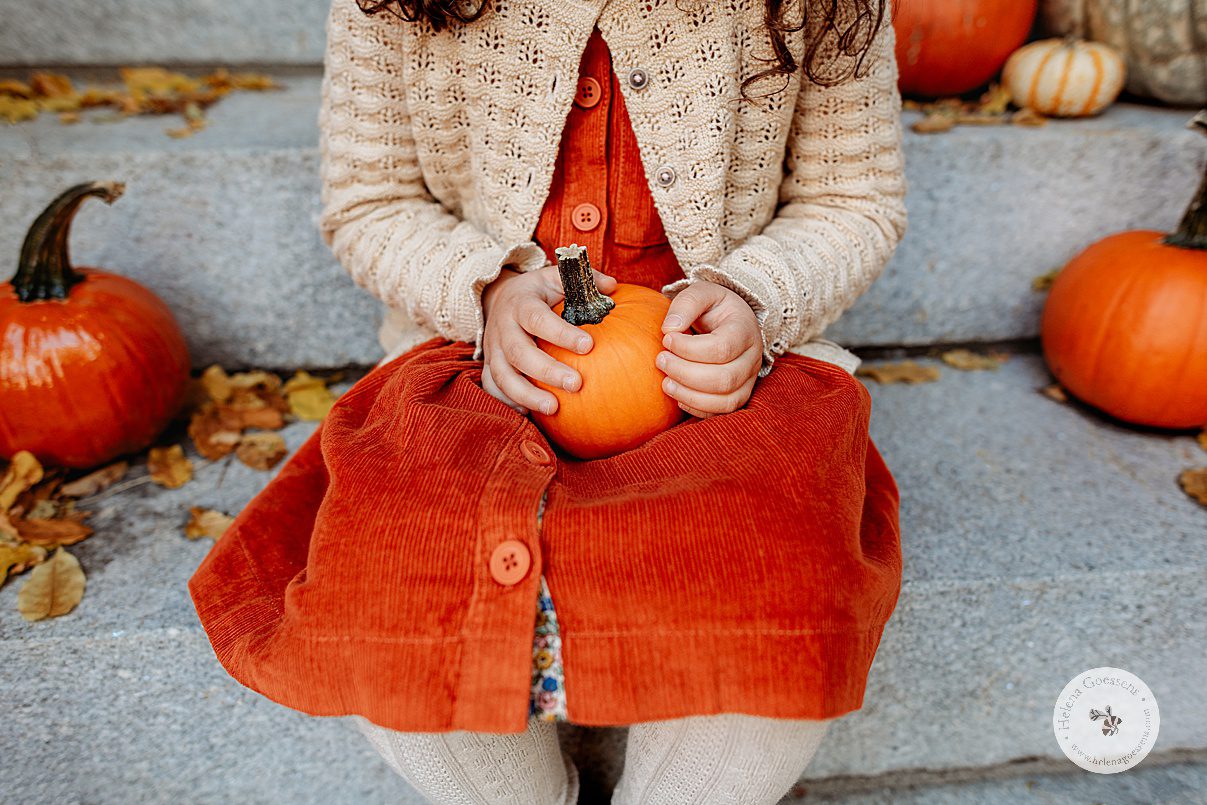 long girl in orange corduroy dress holds little pumpkin in lap on stone step in Beacon Hill 