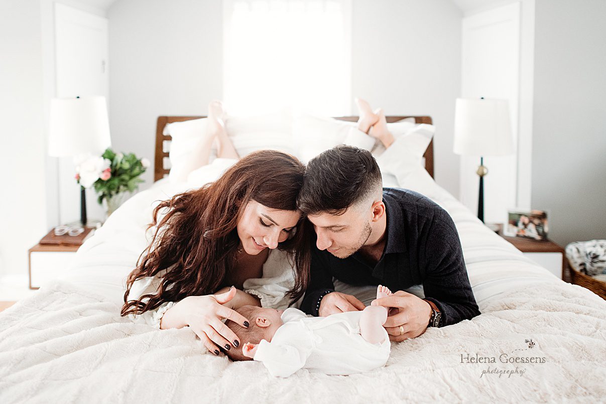 parents lay on stomachs looking newborn son on bed during lifestyle newborn portraits in Waltham MA