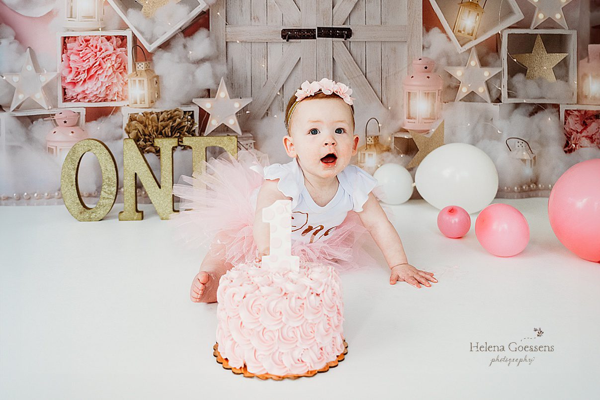 one year old girl reaches for pink icing on cake during first birthday Twinkle Twinkle Little Star cake smash with pink, gold, and white details 