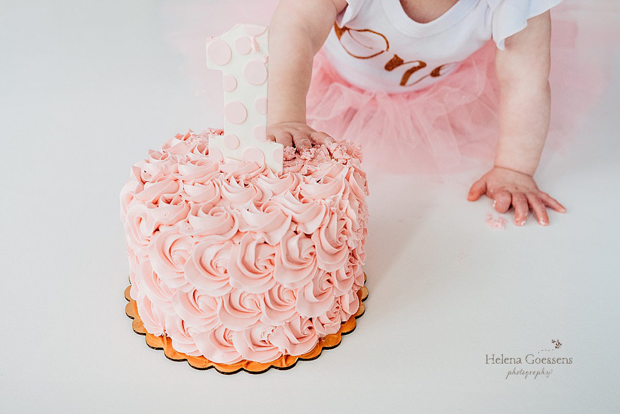 baby leans to put hand in icing on pink cake during Dover MA cake smash 