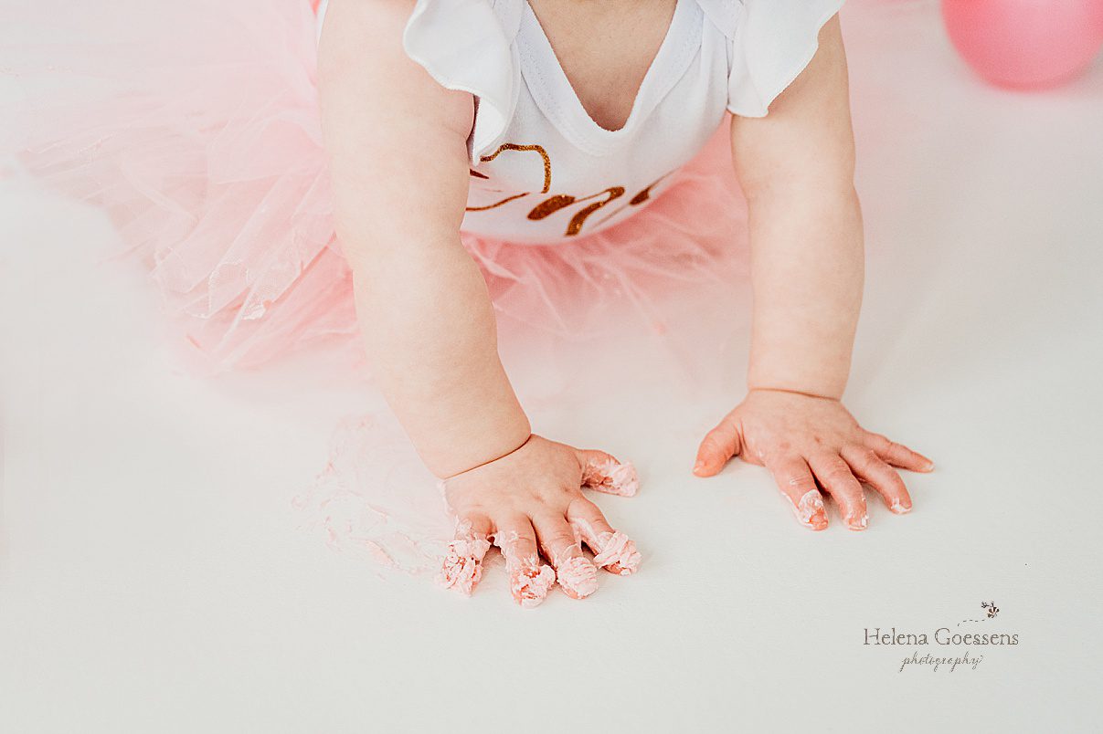 closeup of baby's hand with pink icing on white floor in Dover MA