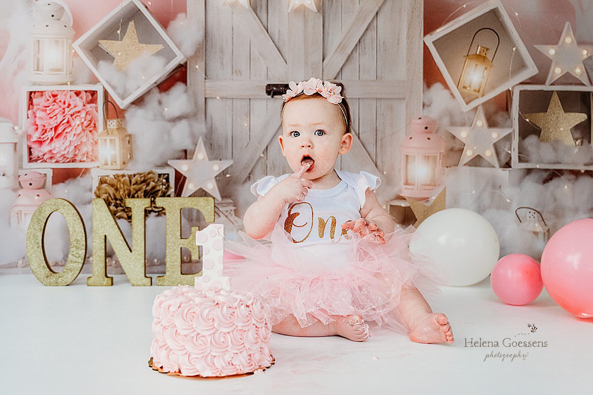 baby licks icing off finger during first birthday Twinkle Twinkle Little Star cake smash with pink, gold, and white details 