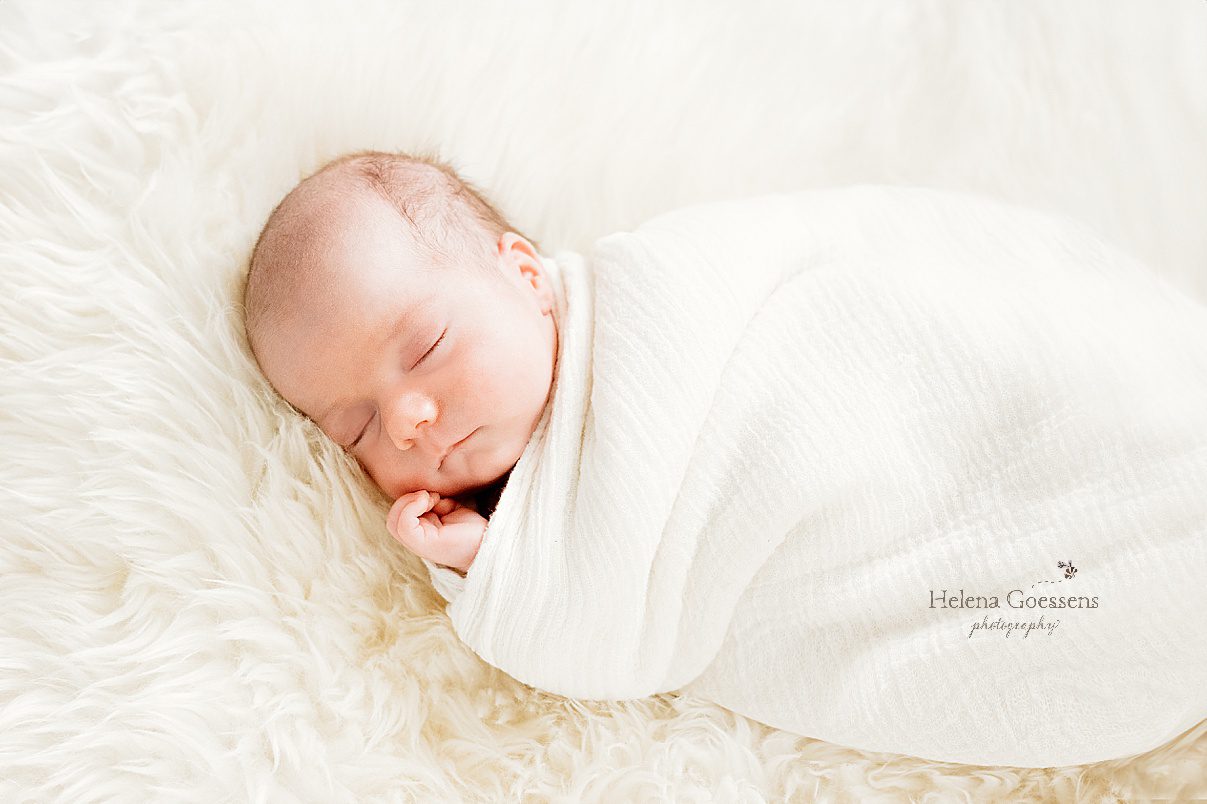 baby sleeps in ivory wrap laying on fuzzy blanket during newborn portraits 