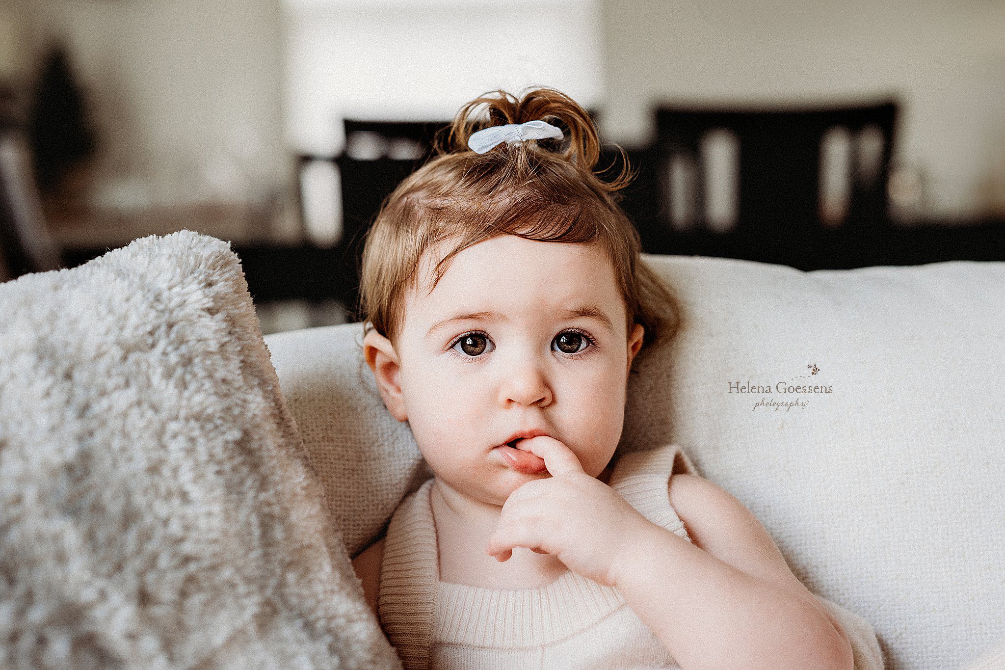 toddler sits on couch with hand in her mouth staring at camera in Boston MA