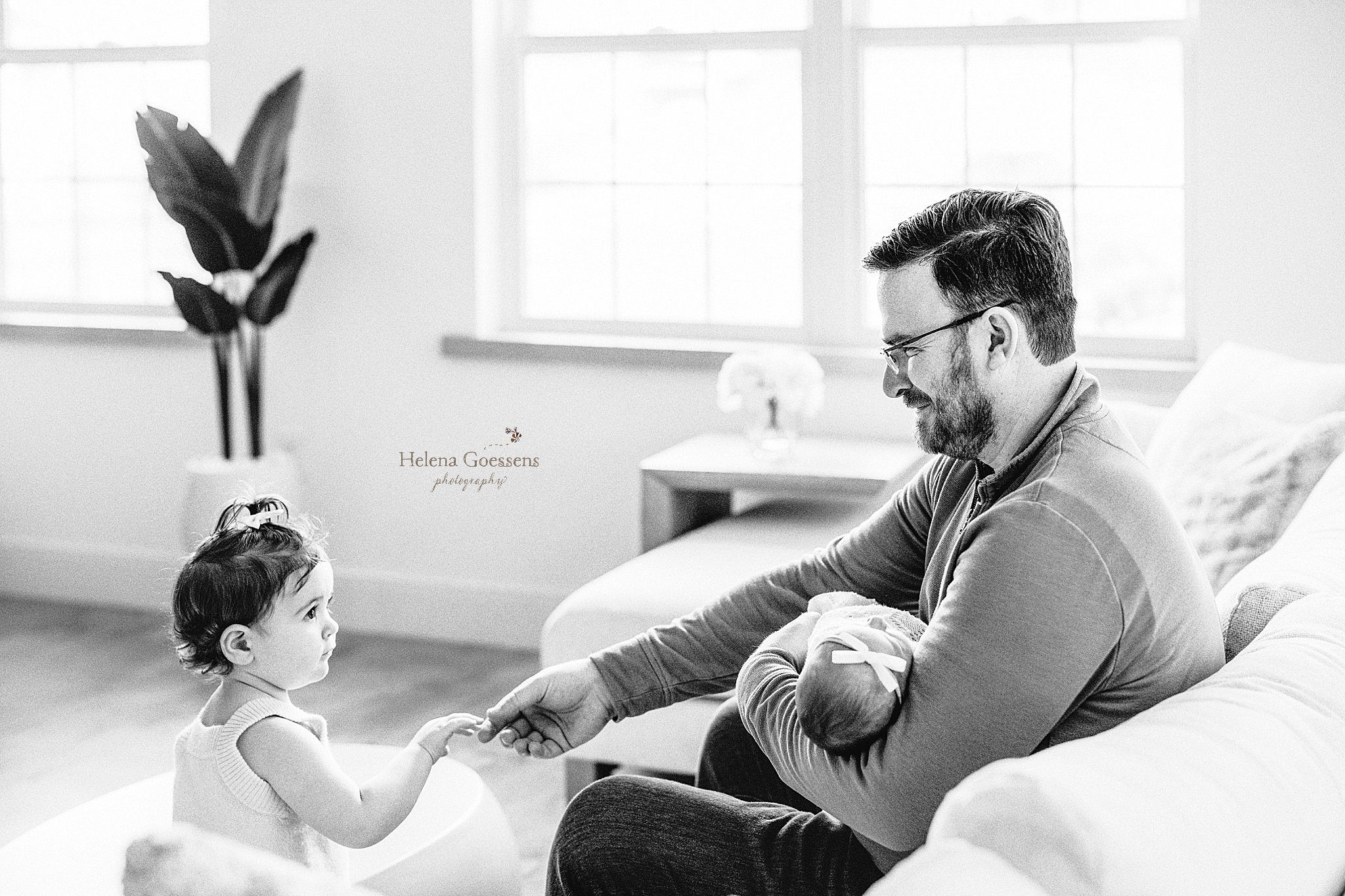 dad holds baby girl while playing with toddler daughter during at home newborn portraits in Canton MA