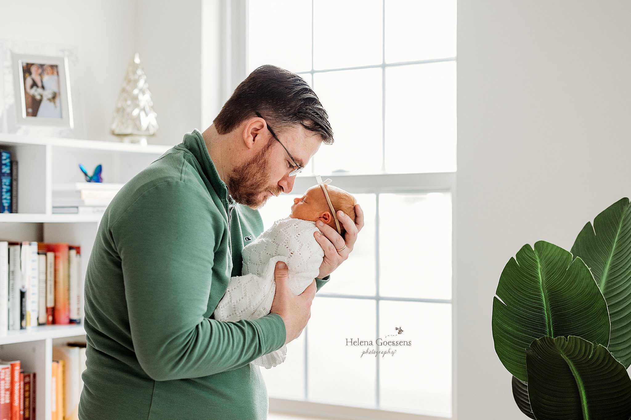 dad holds newborn daughter in front of his chest leaning to her nose during at home newborn portraits in Canton MA